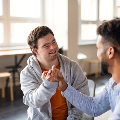 Ein junger, glücklicher Mann mit Down-Syndrom feiert mit seinem betreuenden Freund drinnen in der Schule Erfolge.